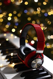 Headphones on electric piano against Christmas tree with blurred lights, closeup. Bokeh effect