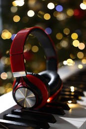 Photo of Headphones on electric piano against Christmas tree with blurred lights, closeup. Bokeh effect