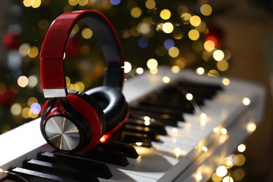 Photo of Headphones on electric piano against Christmas tree with blurred lights, closeup. Bokeh effect