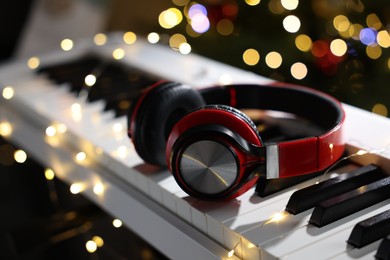 Photo of Headphones on electric piano against blurred lights, closeup. Bokeh effect