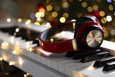 Photo of Headphones on electric piano against Christmas tree with blurred lights, closeup. Bokeh effect