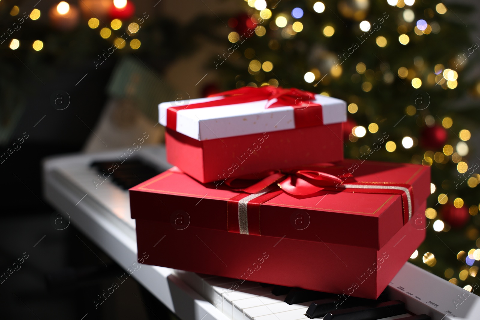 Gifts on electric piano against Christmas tree with blurred lights, closeup. Bokeh effect Photo of Gifts on electric piano against Christmas tree with blurred lights, closeup. Bokeh effect