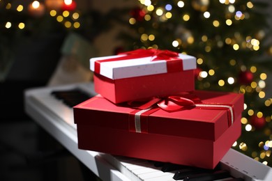 Photo of Gifts on electric piano against Christmas tree with blurred lights, closeup. Bokeh effect