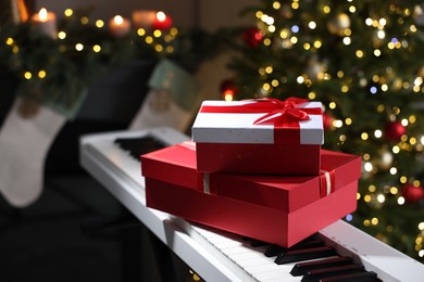 Photo of Gifts on electric piano against Christmas tree with blurred lights, closeup. Bokeh effect