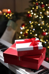 Photo of Gifts on electric piano against Christmas tree with blurred lights, closeup. Bokeh effect