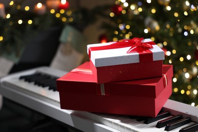 Photo of Gifts on electric piano against Christmas tree with blurred lights, closeup. Bokeh effect