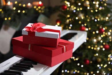 Photo of Gifts on electric piano against Christmas tree with blurred lights, closeup. Bokeh effect