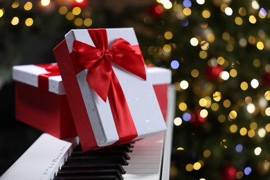 Photo of Gifts on electric piano against Christmas tree with blurred lights, closeup. Bokeh effect