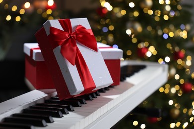 Photo of Gifts on electric piano against Christmas tree with blurred lights, closeup. Bokeh effect