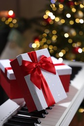 Photo of Gifts on electric piano against Christmas tree with blurred lights, closeup. Bokeh effect