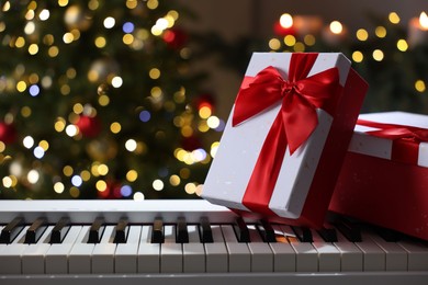 Photo of Gifts on electric piano against Christmas tree with blurred lights, closeup. Bokeh effect