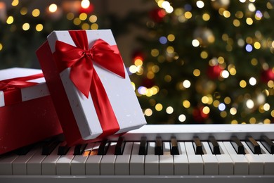 Photo of Gifts on electric piano against Christmas tree with blurred lights, closeup. Bokeh effect