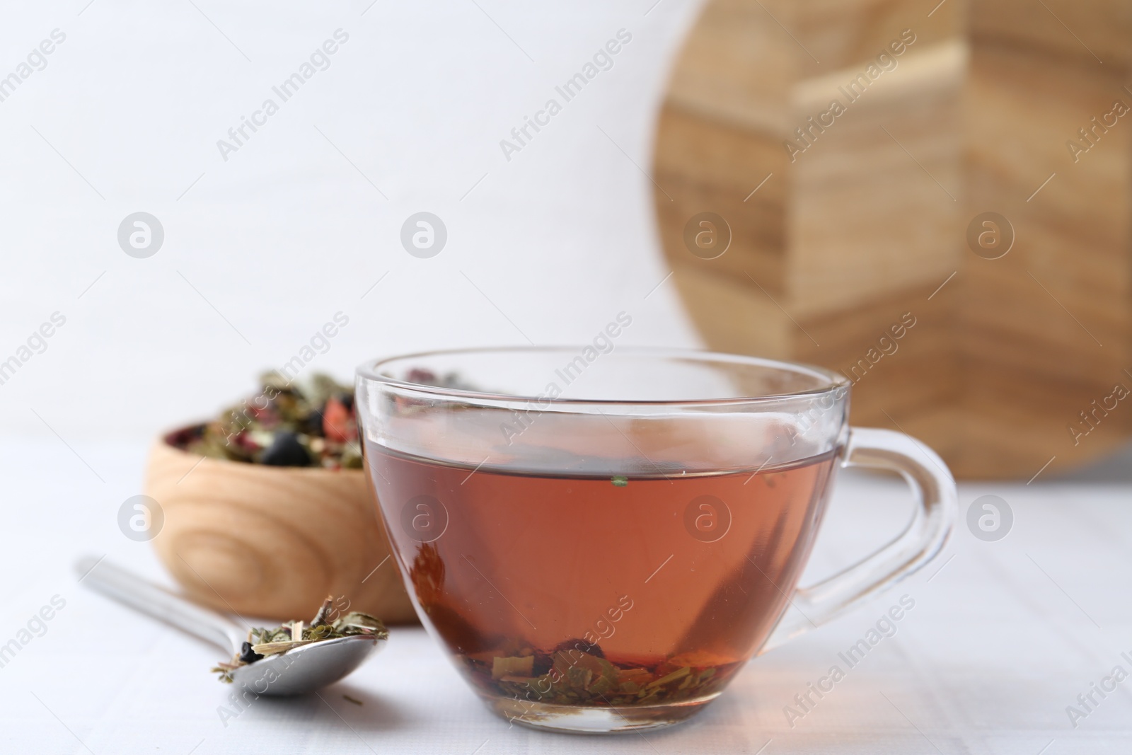 Photo of Delicious herbal tea and dry leaves on white tiled table, closeup