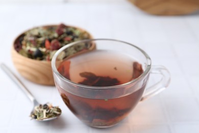 Photo of Delicious herbal tea and dry leaves on white tiled table, closeup