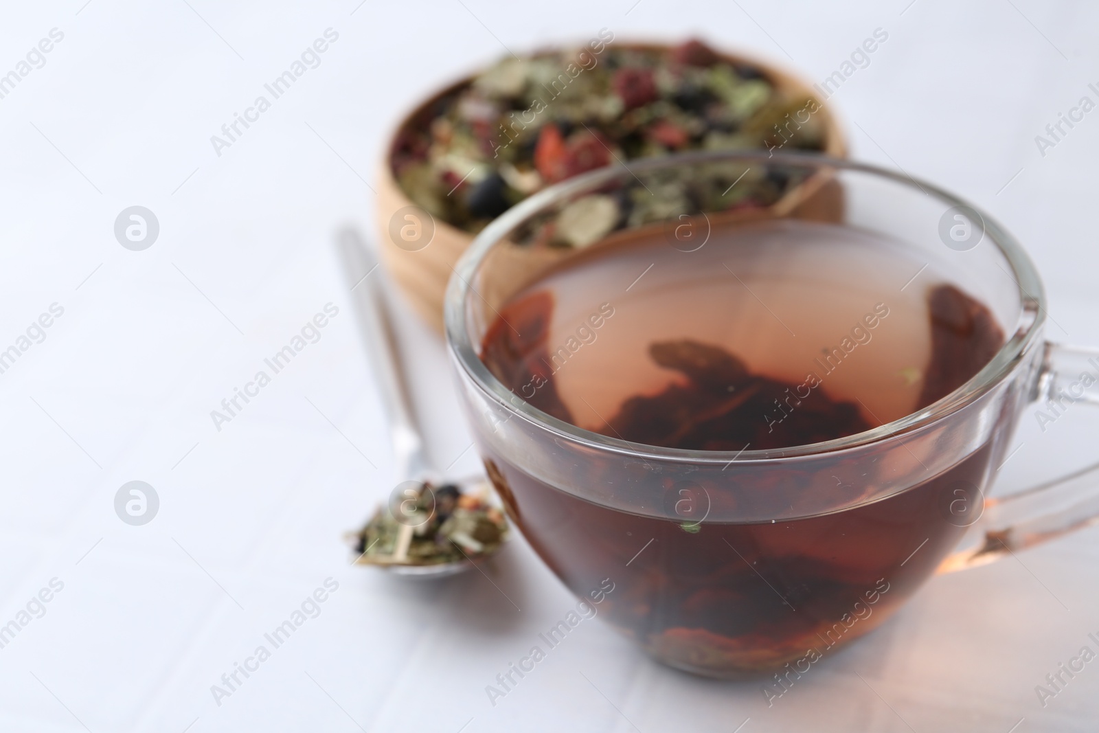 Photo of Delicious herbal tea and dry leaves on white tiled table, closeup