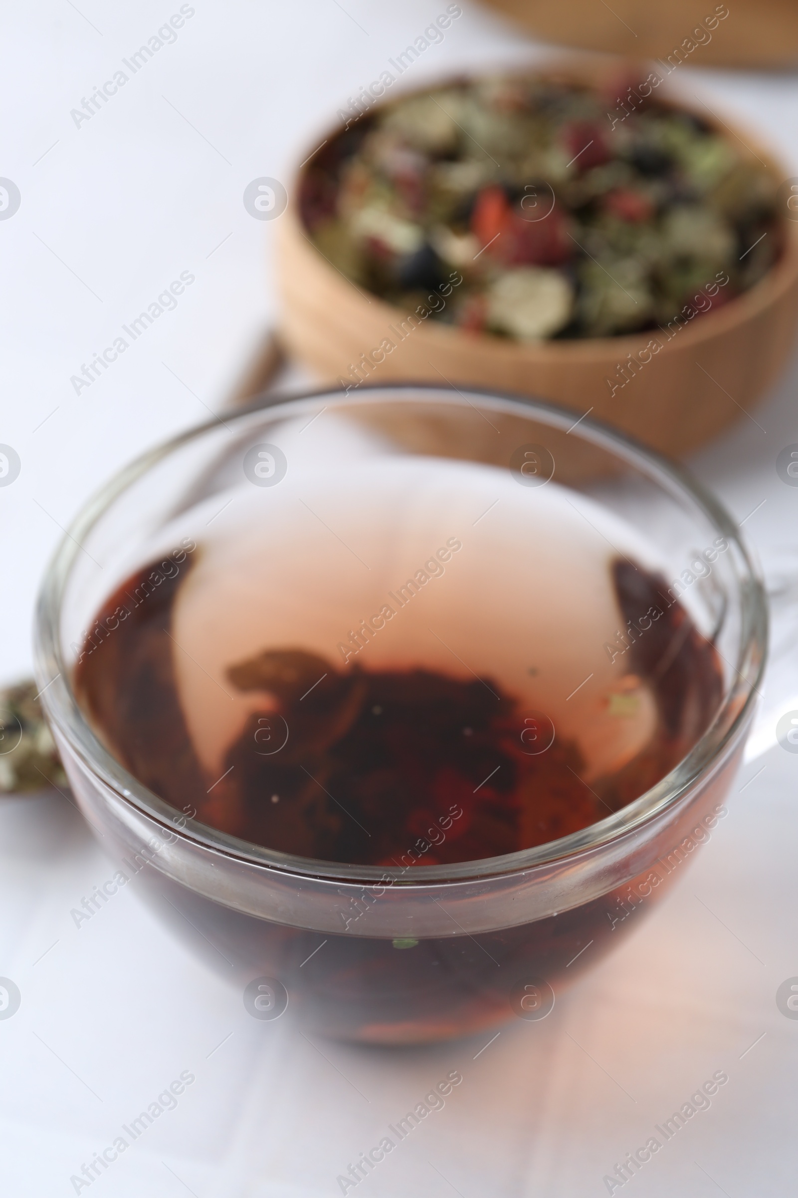 Photo of Delicious herbal tea and dry leaves on white tiled table, closeup