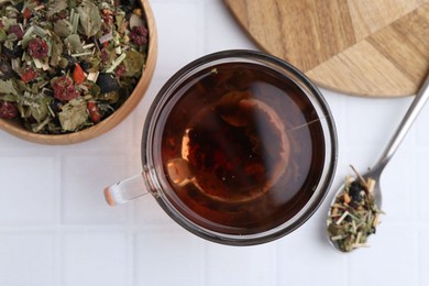 Photo of Delicious herbal tea and dry leaves on white tiled table, flat lay