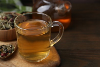 Photo of Delicious herbal tea and dry leaves on wooden table, closeup. Space for text