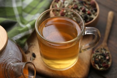 Photo of Delicious herbal tea and dry leaves on wooden table, closeup