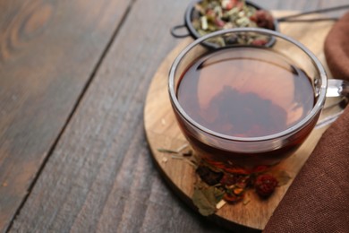 Photo of Delicious herbal tea and dry leaves on wooden table, closeup. Space for text