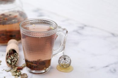 Photo of Delicious herbal tea with honey and dry leaves on white marble table, closeup. Space for text