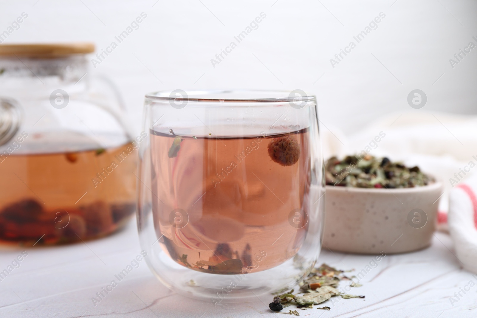 Photo of Delicious herbal tea and dry leaves on white table, closeup