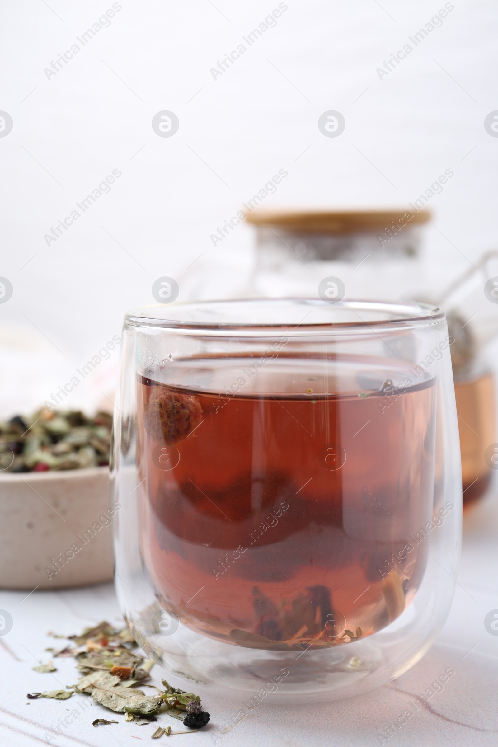 Photo of Delicious herbal tea and dry leaves on white table, closeup