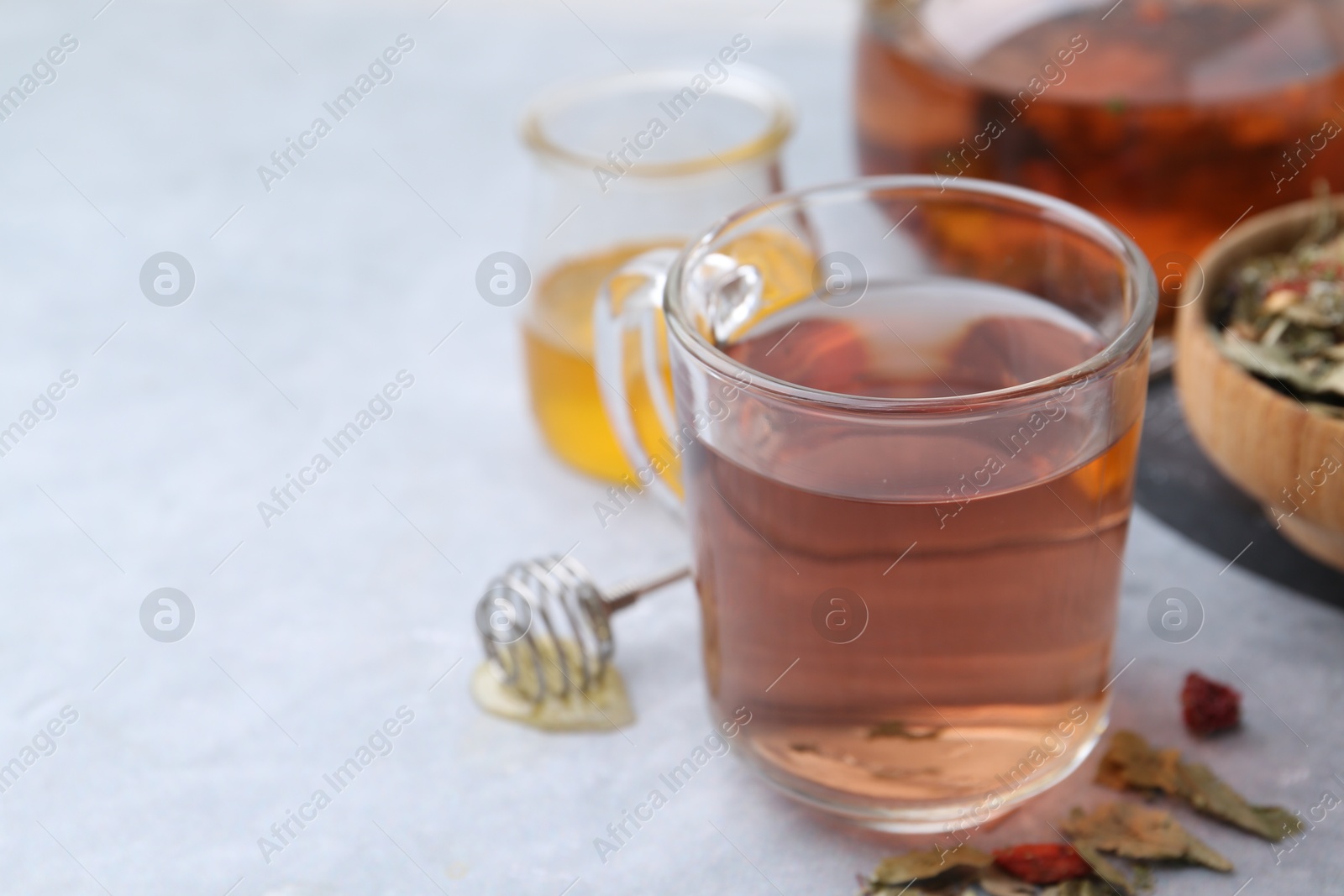 Photo of Delicious herbal tea with honey and dry leaves on grey table, closeup. Space for text