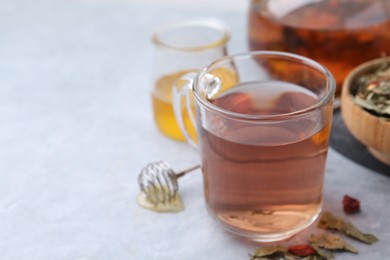 Photo of Delicious herbal tea with honey and dry leaves on grey table, closeup. Space for text