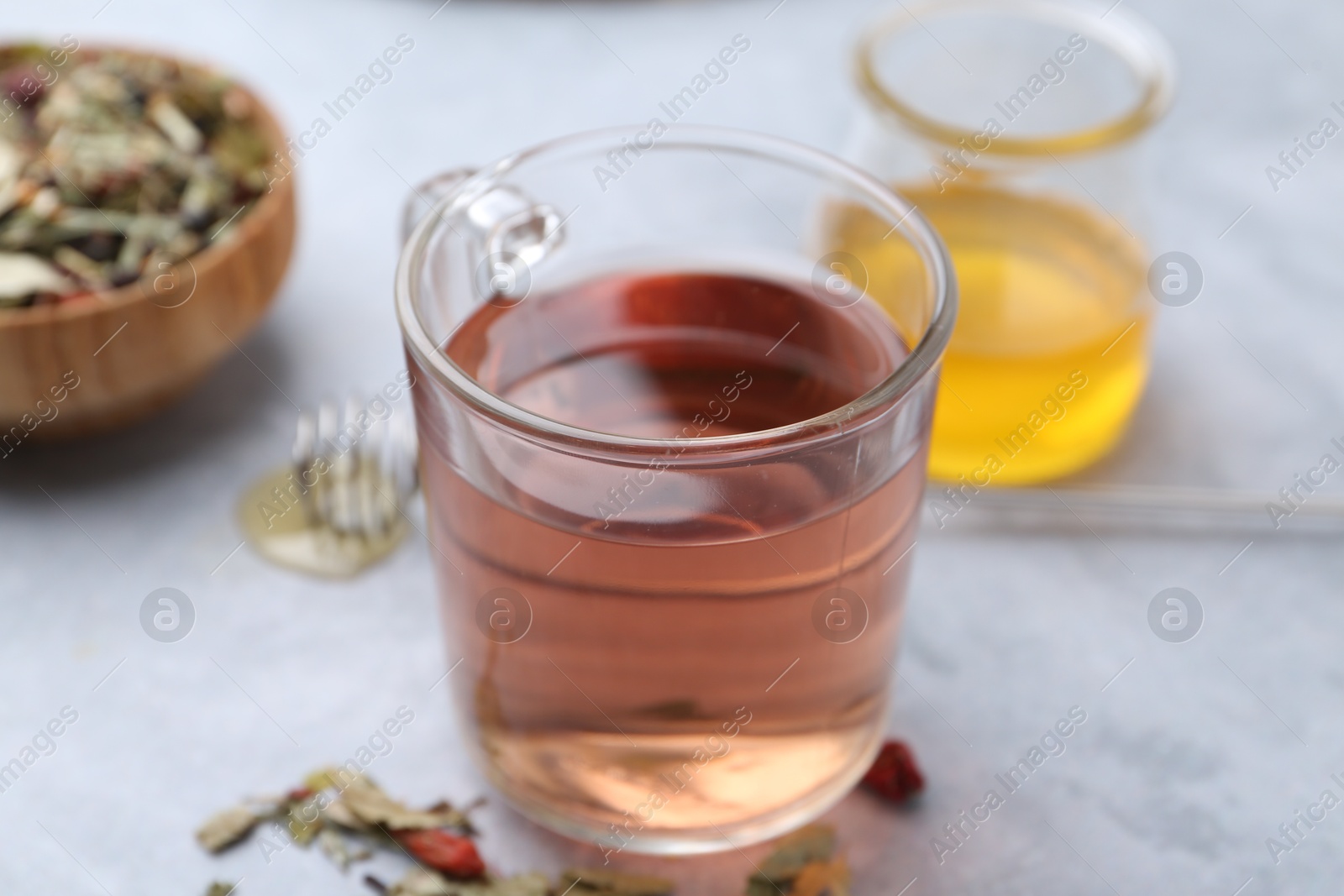 Photo of Delicious herbal tea and dry leaves on grey table, closeup