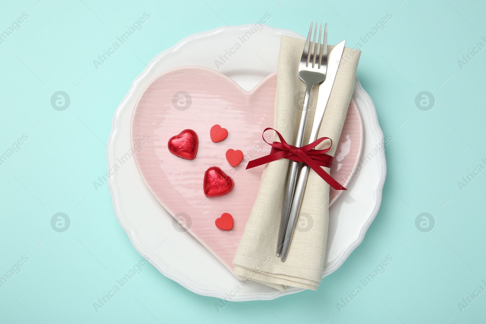 Photo of Romantic place setting with cutlery and plates on light blue background, top view. Valentine's day celebration