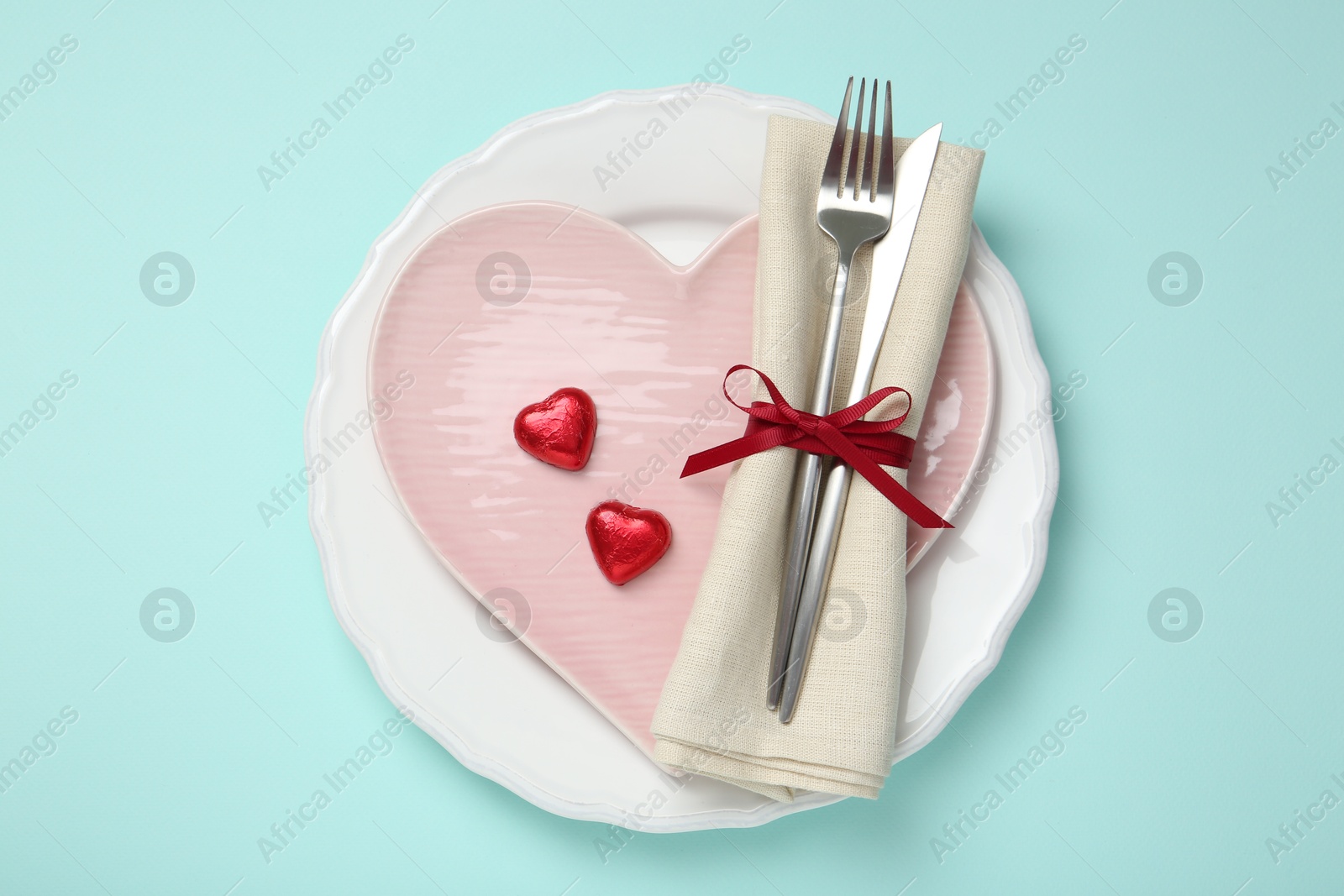 Photo of Romantic place setting with cutlery and plates on light blue background, top view. Valentine's day celebration