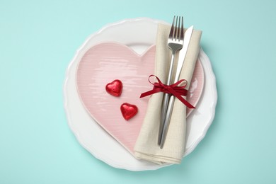 Photo of Romantic place setting with cutlery and plates on light blue background, top view. Valentine's day celebration