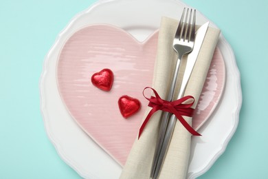 Photo of Romantic place setting with cutlery and plates on light blue background, top view. Valentine's day celebration