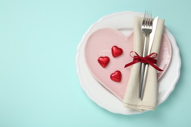 Photo of Valentine's day celebration. Romantic place setting with cutlery and plates on light blue background, top view. Space for text