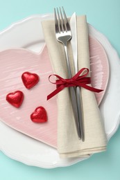 Photo of Romantic place setting with cutlery and plates on light blue background, top view. Valentine's day celebration