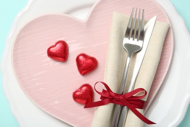 Photo of Romantic place setting with cutlery and plates on light blue background, top view. Valentine's day celebration