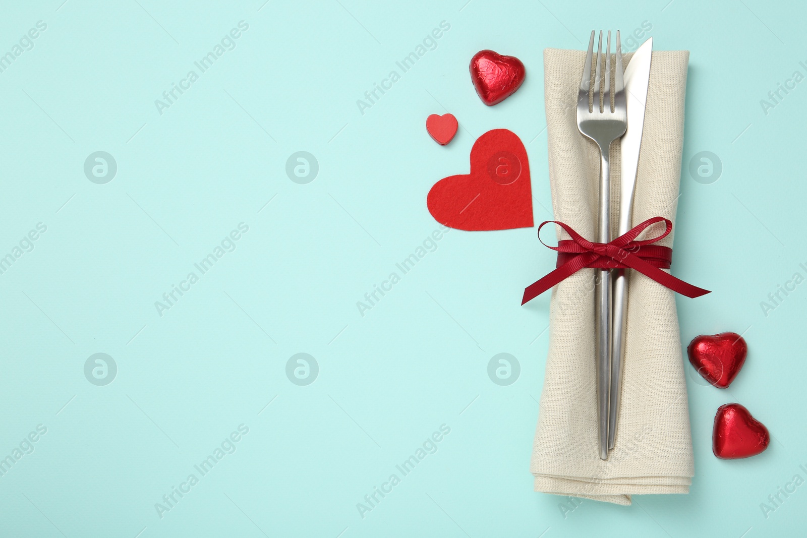 Photo of Valentine's day celebration. Romantic place setting with cutlery and hearts on light blue background, flat lay. Space for text