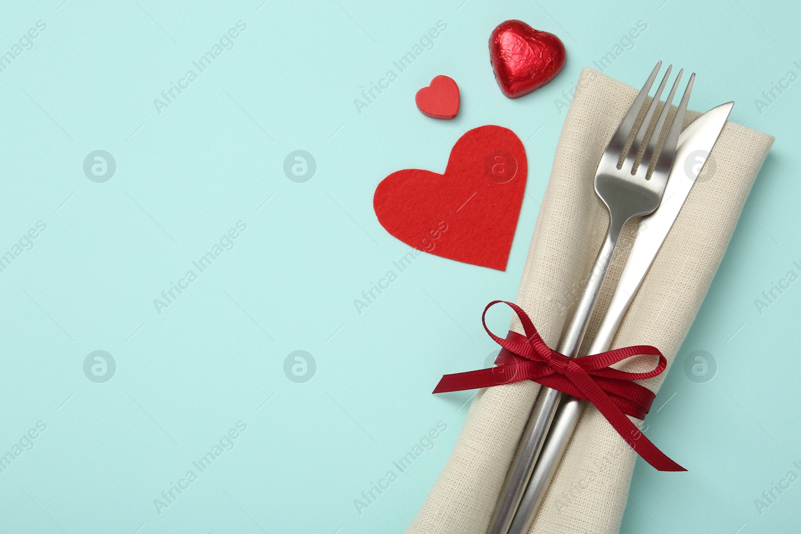 Photo of Valentine's day celebration. Romantic place setting with cutlery and hearts on light blue background, flat lay. Space for text