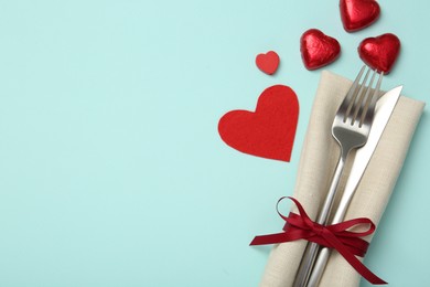 Photo of Valentine's day celebration. Romantic place setting with cutlery and hearts on light blue background, flat lay. Space for text