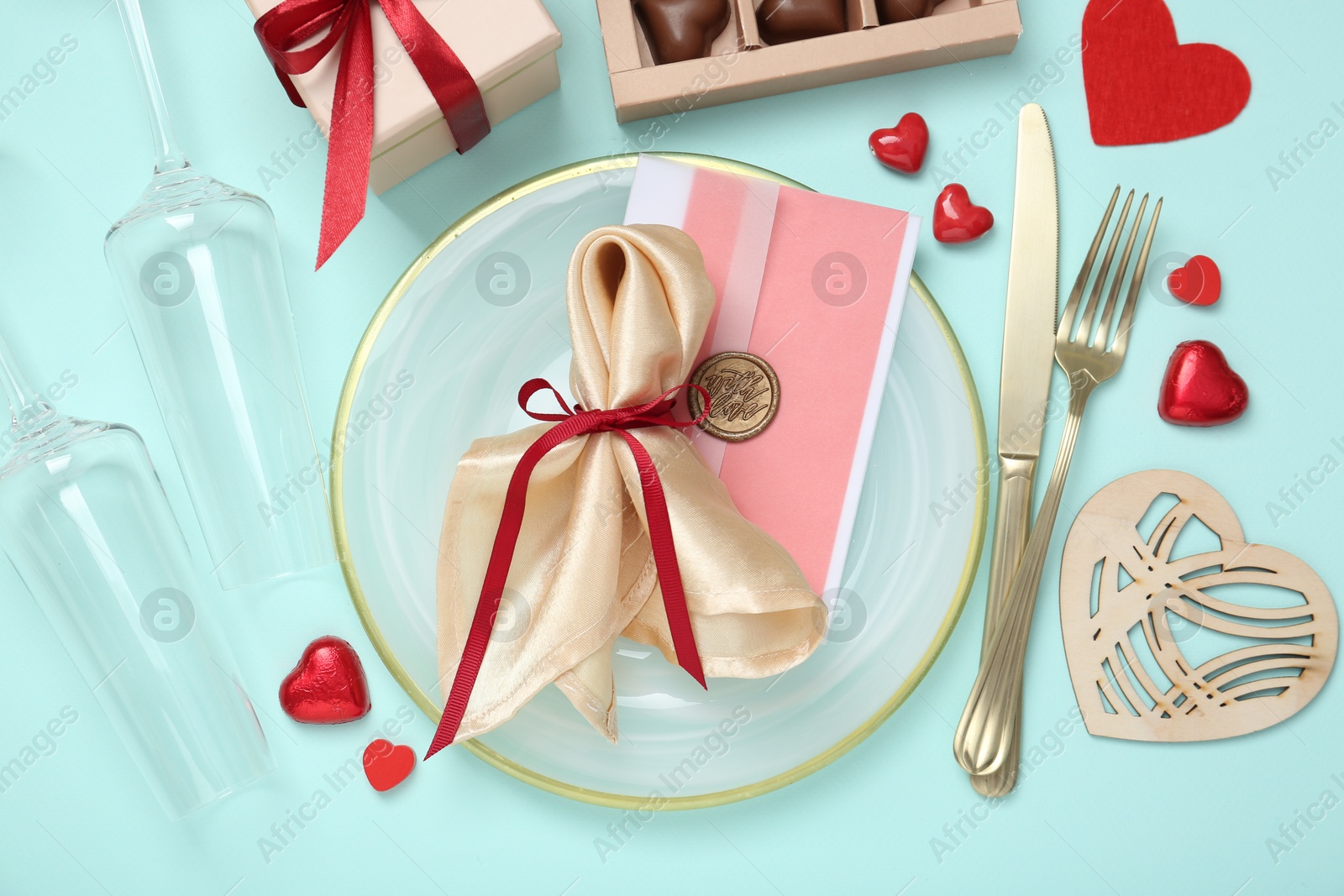 Photo of Romantic place setting with cutlery, hearts, glasses and candies on light blue background, flat lay. Valentine's day celebration