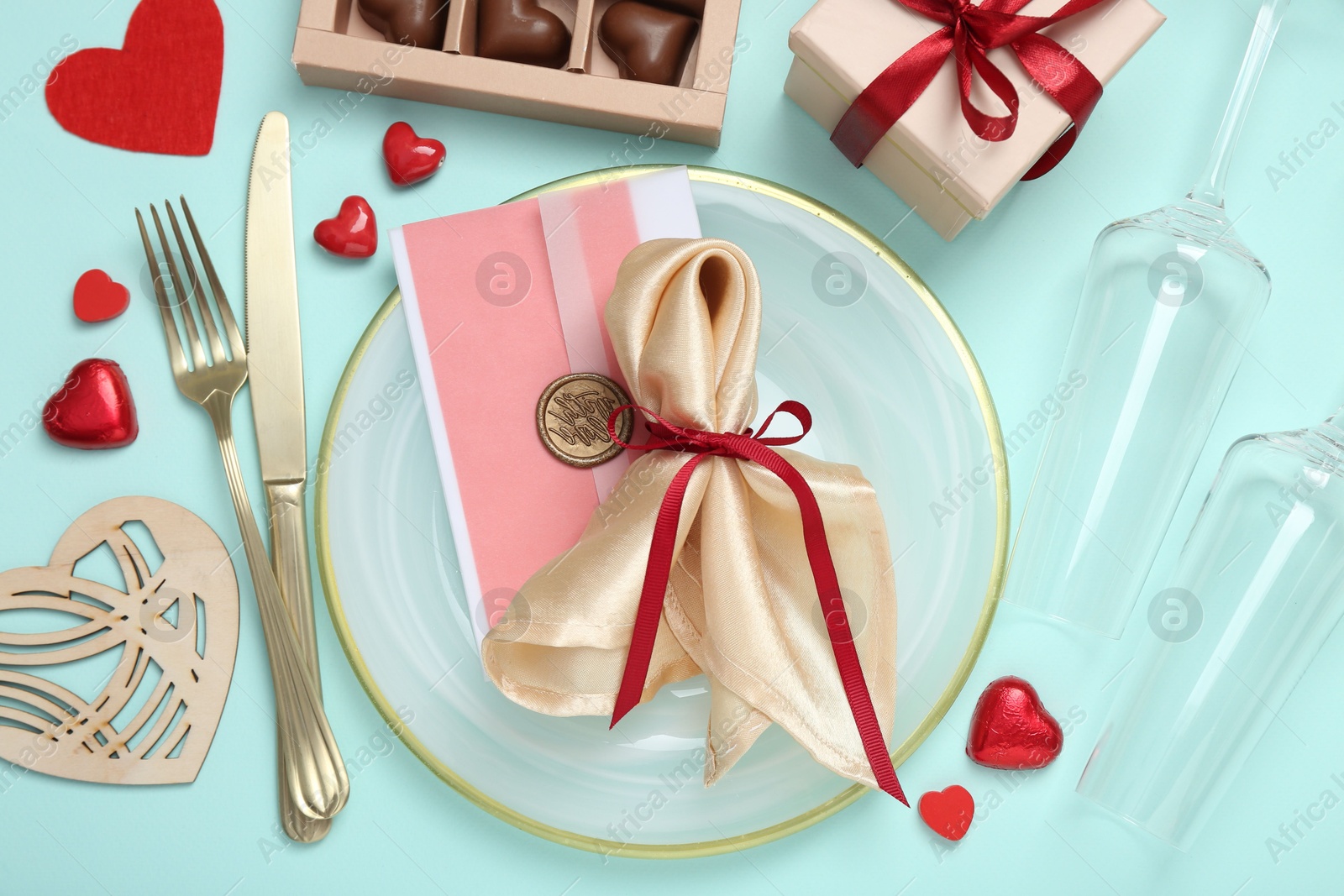 Photo of Romantic place setting with cutlery, hearts, glasses and candies on light blue background, flat lay. Valentine's day celebration