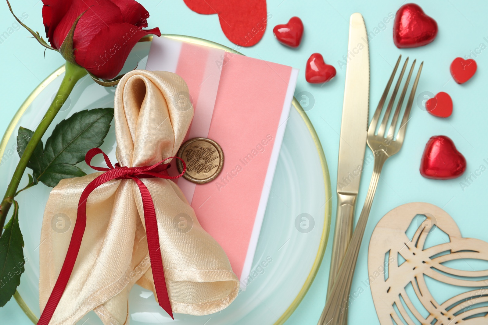 Photo of Romantic place setting with cutlery, hearts and red rose on light blue background, flat lay. Valentine's day celebration