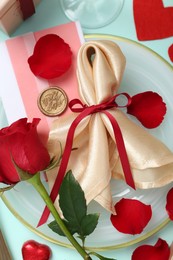 Photo of Romantic place setting with napkin, petals and red rose on light blue background, flat lay. Valentine's day celebration