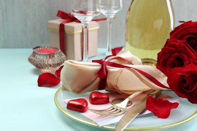 Photo of Valentine's day celebration. Romantic place setting with cutlery, hearts and red roses on light blue table, closeup. Space for text