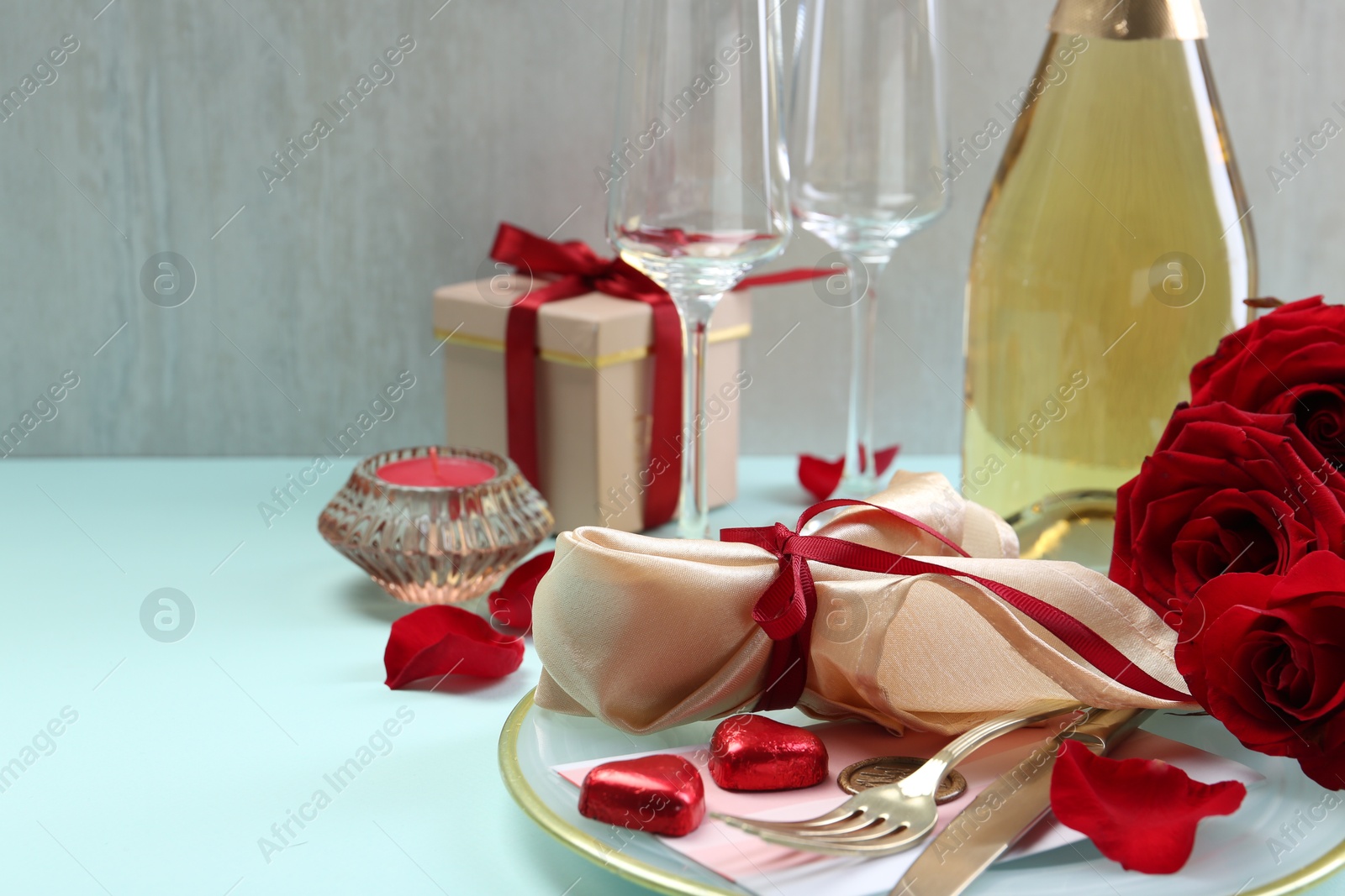 Photo of Valentine's day celebration. Romantic place setting with cutlery, hearts and red roses on light blue table, closeup. Space for text