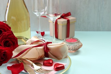 Photo of Valentine's day celebration. Romantic place setting with cutlery, hearts and red roses on light blue table, closeup. Space for text