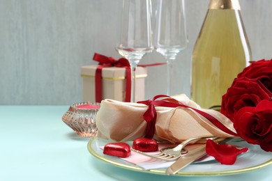 Photo of Valentine's day celebration. Romantic place setting with cutlery, hearts and red roses on light blue table, closeup. Space for text