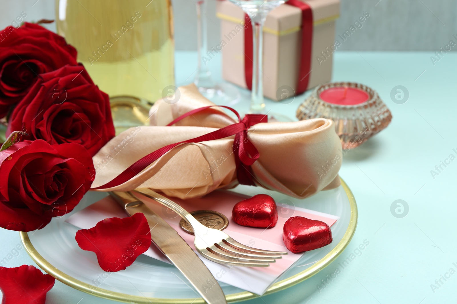 Photo of Valentine's day celebration. Romantic place setting with cutlery, hearts and red roses on light blue table, closeup. Space for text