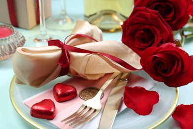 Romantic place setting with cutlery, hearts and red roses on light blue background, closeup. Valentine's day celebration